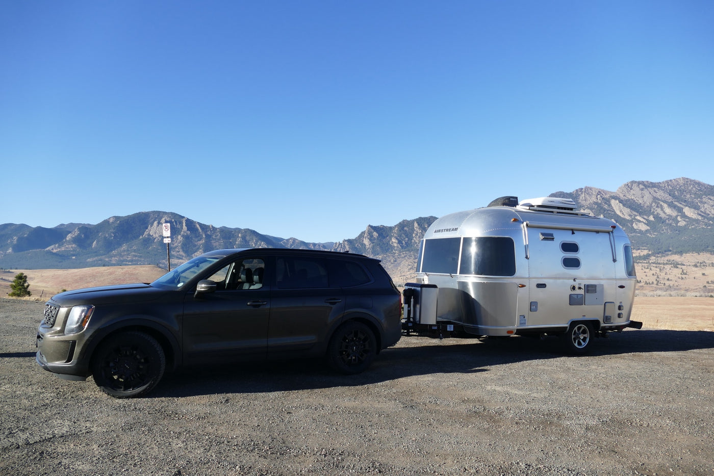 Dark SUV towing a shiny Airstream rv rental on gravel. Mountains and clear blue sky in background, perfect for a travel adventure. — photo 4