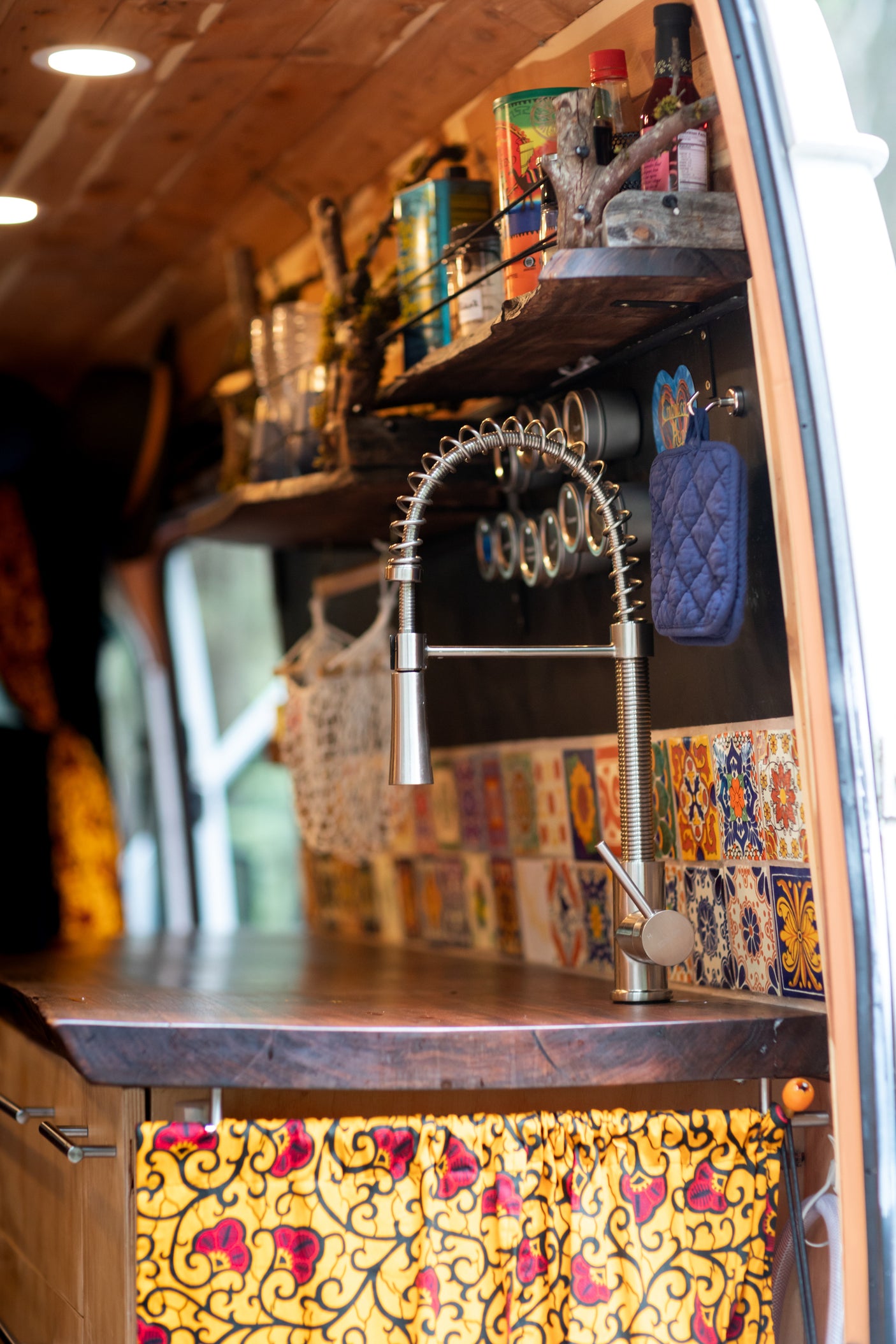 Inside an RV rental: a stylish kitchen featuring a modern faucet, wooden counter, colorful tiled backsplash, and unique curtain storage.