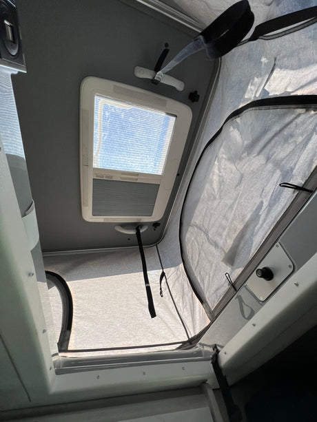 Experience an RV rental: Interior view of a pop-top camper with skylight and light-filled fabric tent extension.