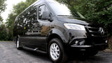 A sleek black Mercedes-Benz Sprinter van, ideal for a luxury trip or RV rental, reflecting trees and another vehicle.