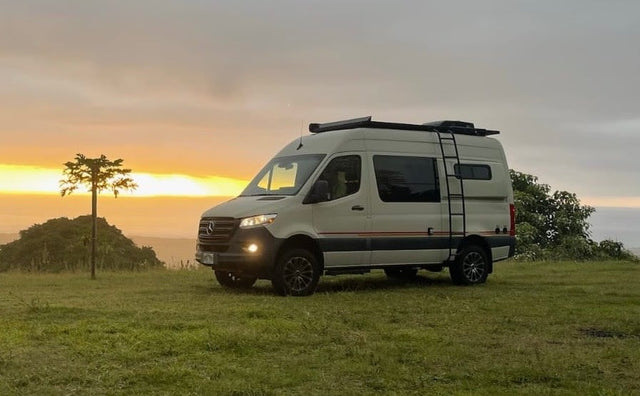 Scenic **rv rental**: A light-colored Mercedes Sprinter **camper van** enjoys a beautiful **sunset** from a grassy hilltop overlooking the ocean.|Inside a modern RV rental camper van