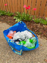 Blue IKEA bag with colorful inflatables on concrete near a garden of red tulips and a wooden fence, great for an RV rental trip.