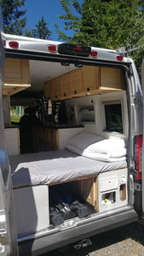 Open back of a custom camper van RV rental. See the comfy bed, kitchen, and wooden cabinets inside.