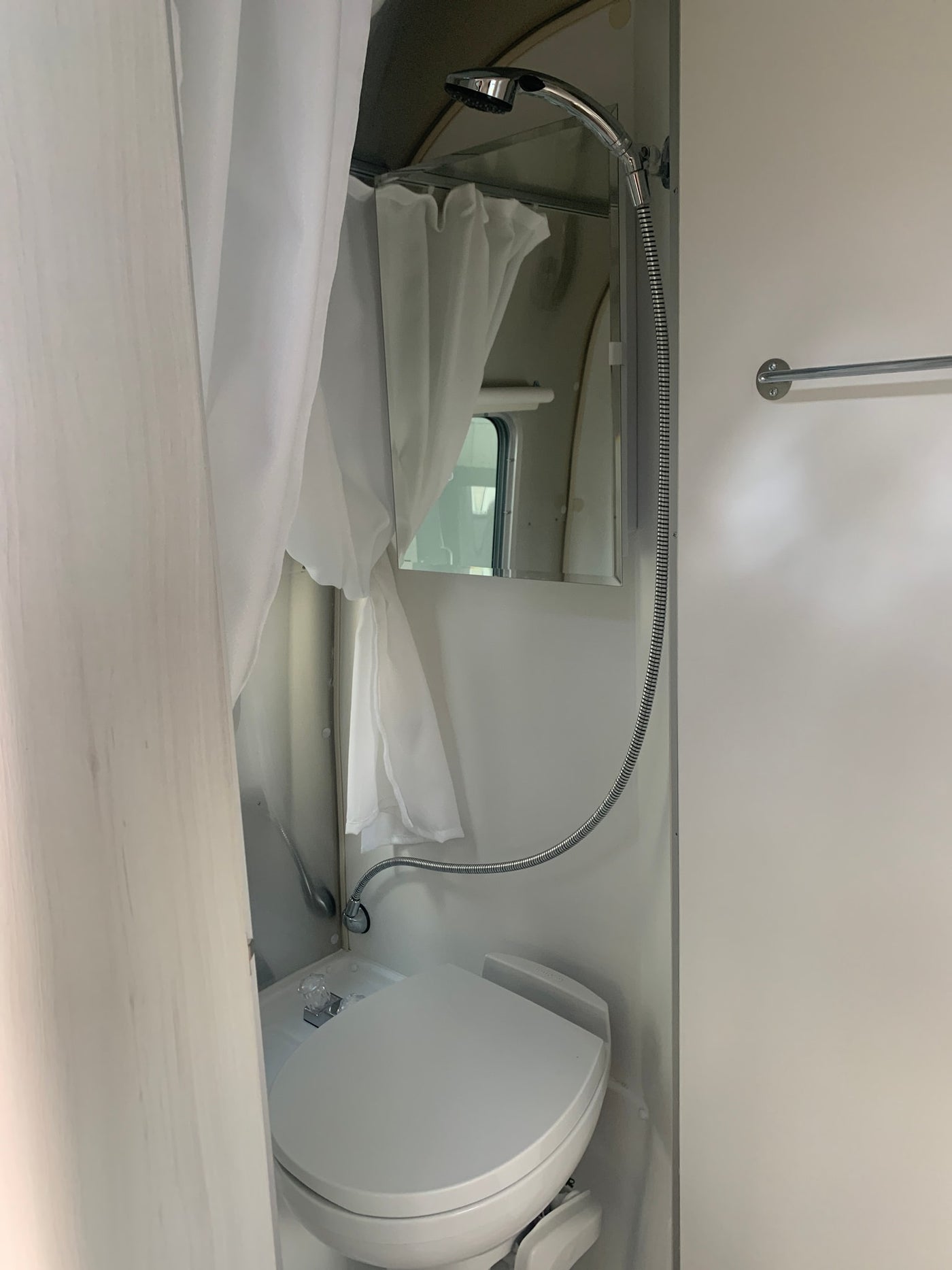 Compact RV rental bathroom: hand-held shower, mirror, window, and wall-mounted toilet. — photo 8