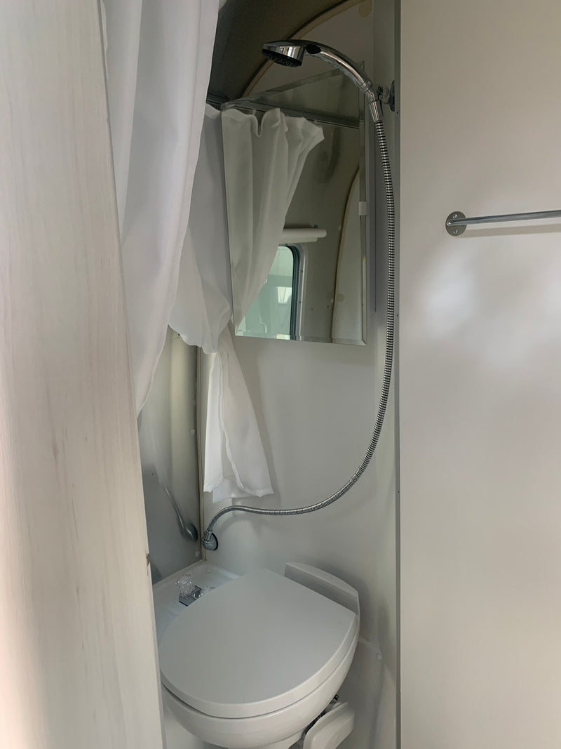 Compact RV rental bathroom: hand-held shower, mirror, window, and wall-mounted toilet. — photo 8