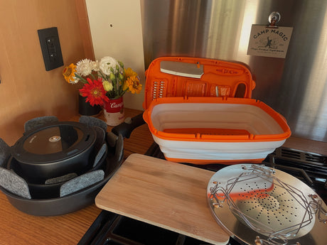 Compact camping kitchen setup in an RV rental, featuring nested pots, a cutting board, and cooking tools for outdoor experiences.