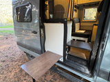 RV rental's open side reveals an outdoor table, cozy seating, and modern interior for travel.