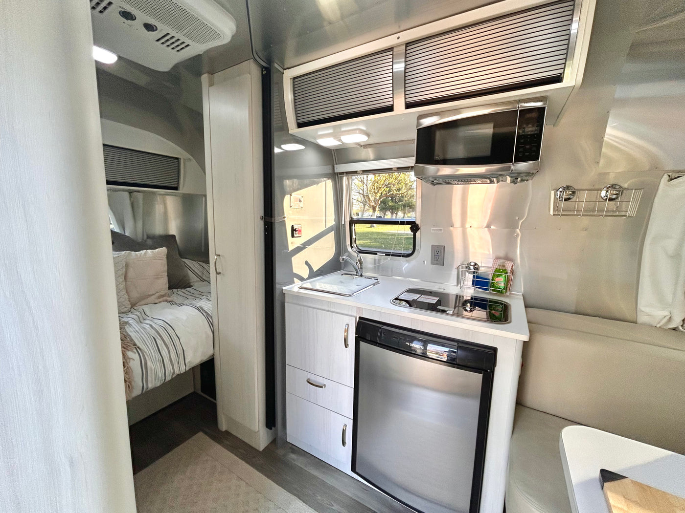 RV rental interior with compact kitchen (microwave, sink, fridge), comfortable bed, and living area. — photo 12