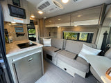 Modern RV rental interior with compact kitchen, sofa seating, and overhead cabinets for storage.
