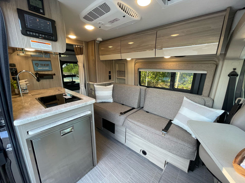 Modern RV rental interior with compact kitchen, sofa seating, and overhead cabinets for storage. — photo 8