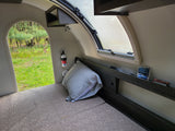 RV rental interior: bed, window, safety gear, and an open archway to a vibrant green forest view.