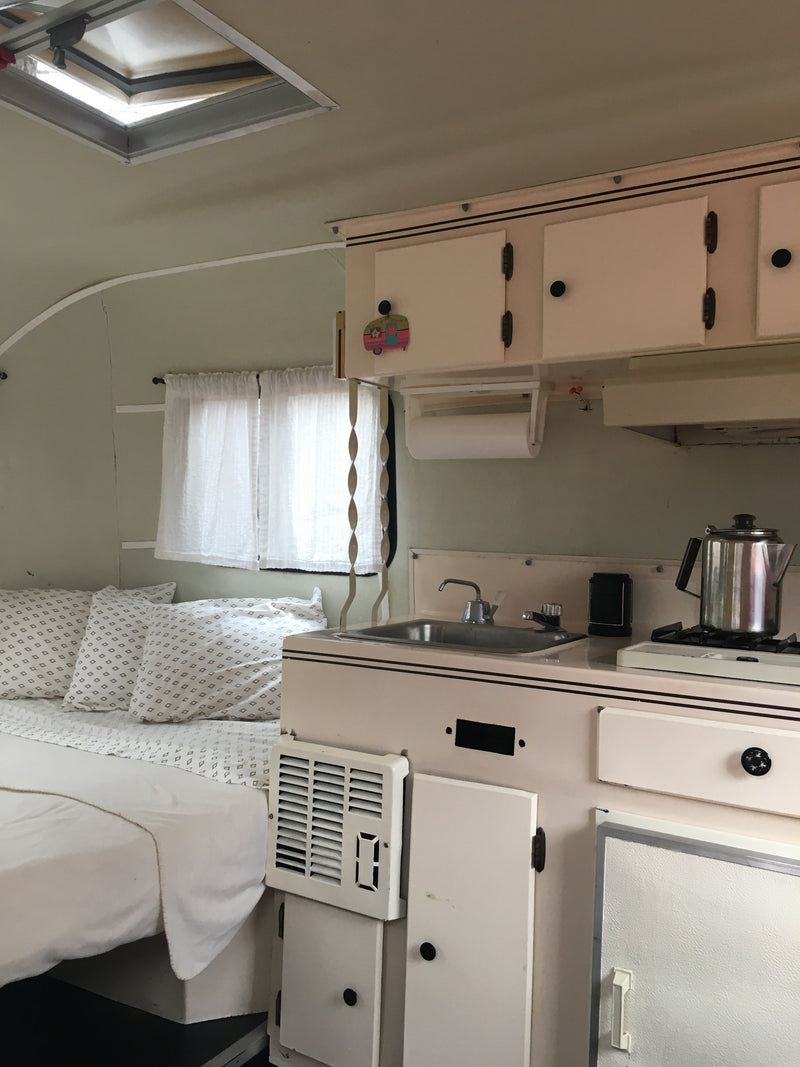 Cozy RV rental interior with bed, compact kitchen, overhead cabinets, and a ceiling vent. — photo 7