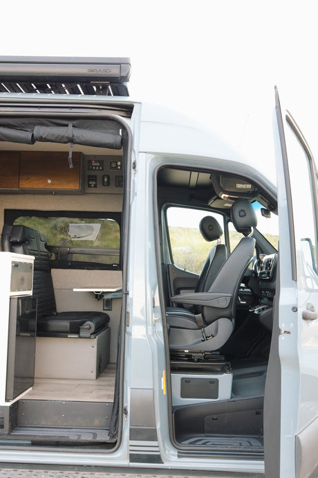 Inside an RV rental campervan: open doors show the driver's cabin and a customized living area with bench seating and controls.