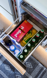 Inside an RV rental: a well-stocked fridge drawer with Poppi sodas, lemons, sparkling water bottles, and canned drinks.