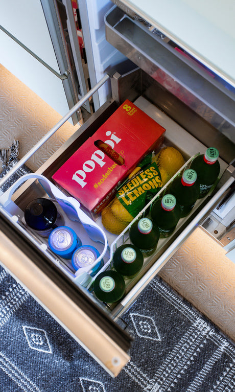Inside an RV rental: a well-stocked fridge drawer with Poppi sodas, lemons, sparkling water bottles, and canned drinks.
