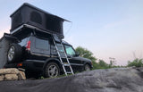 A black Land Rover SUV with a deployed roof-top tent and ladder, parked on rocks, perfect for an rv rental adventure.