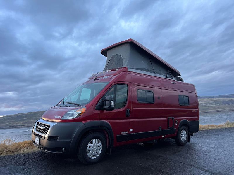  surrounded by dry brush under a cloudy sky.|Red RV rental by a powerful waterfall cascading down a mossy cliff with tall trees. Perfect for a scenic outdoor adventure.|Red RV rental parked at a stunning scenic overlook — photo 3