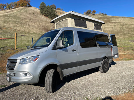 Ready for adventure! A silver Sprinter pop-top camper van, available for RV rental, parked on a scenic hill.