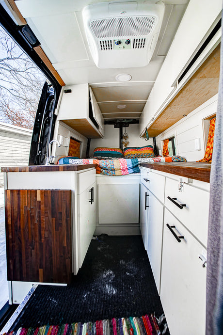 Compact and colorful RV rental interior with a cozy bed, kitchen, and open door, perfect for van life adventures.