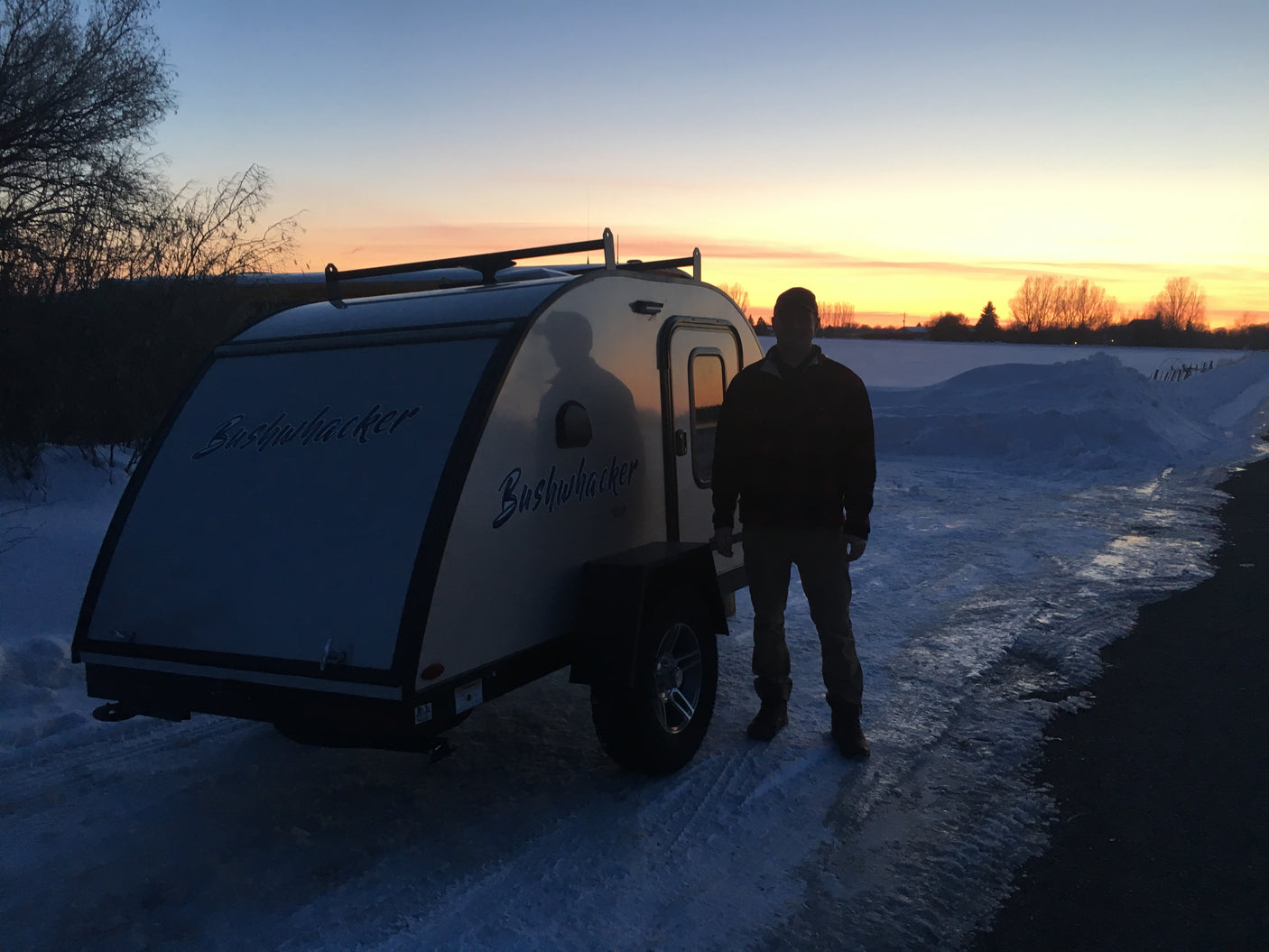 Bushwhacker teardrop RV rental, ready for winter adventures with a man at snowy sunset.