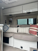 Explore a modern RV rental interior featuring comfortable bench seating, stylish pillows, and convenient overhead cabinets.