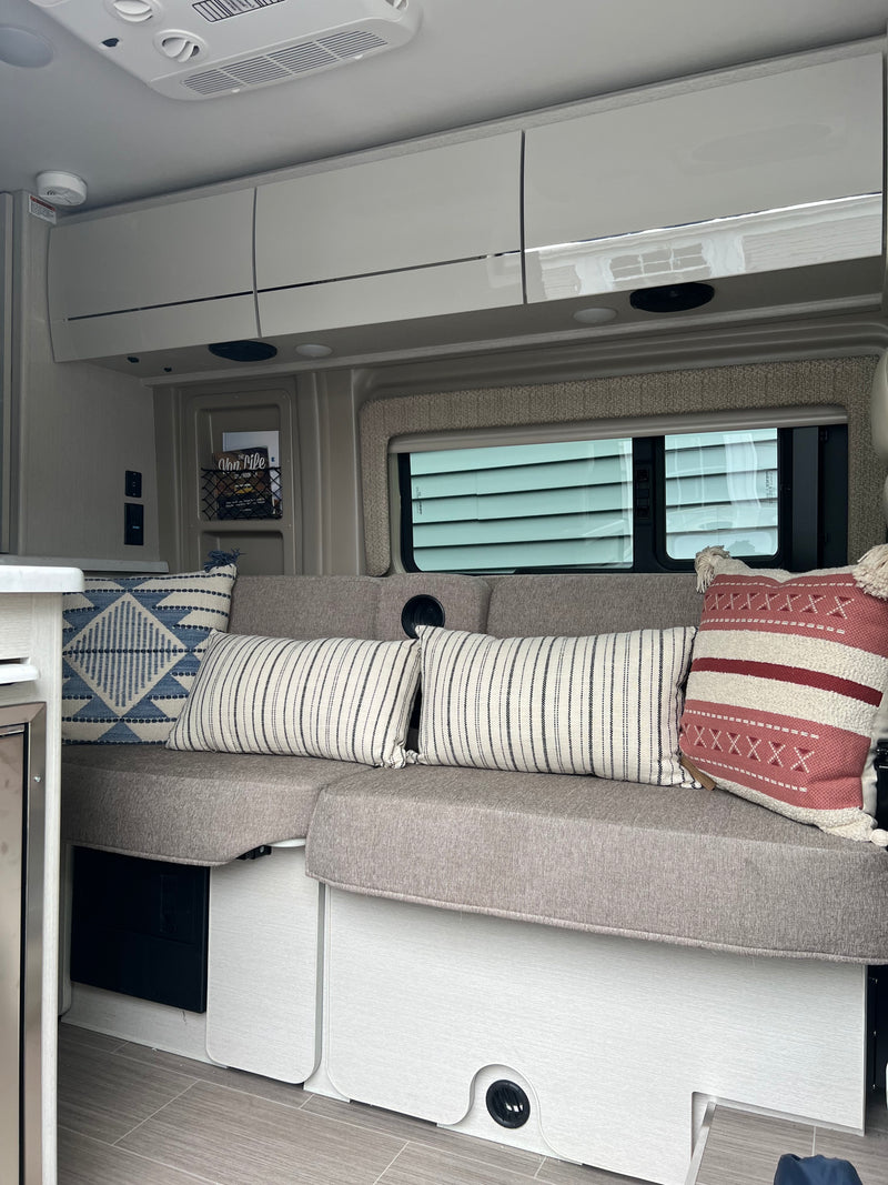 Explore a modern RV rental interior featuring comfortable bench seating, stylish pillows, and convenient overhead cabinets. — photo 13