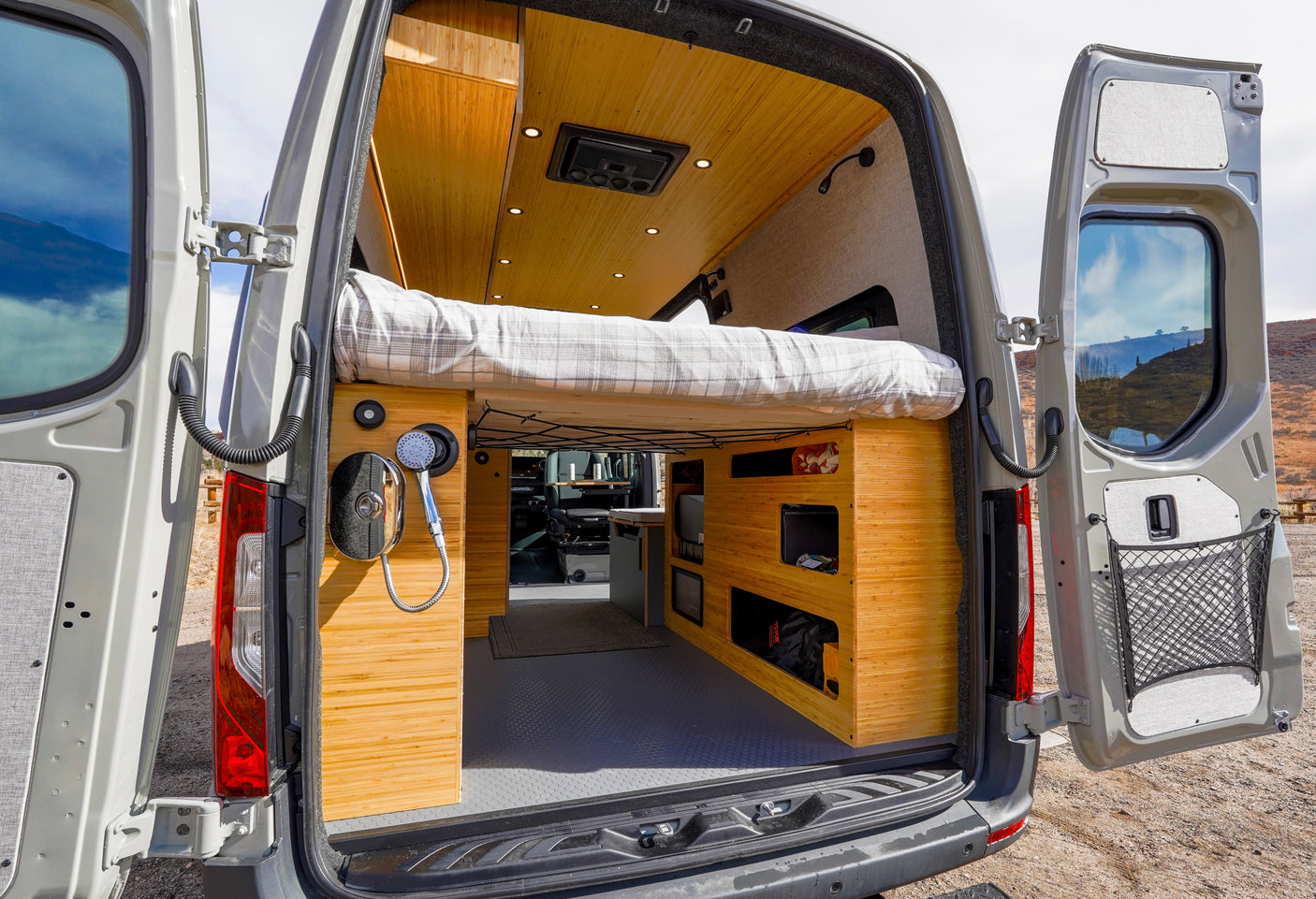 Explore this rv rental camper van's interior: open rear doors reveal a cozy bed, bamboo-style cabinets, and a convenient shower setup.