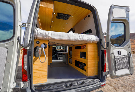 Explore this rv rental camper van's interior: open rear doors reveal a cozy bed, bamboo-style cabinets, and a convenient shower setup.