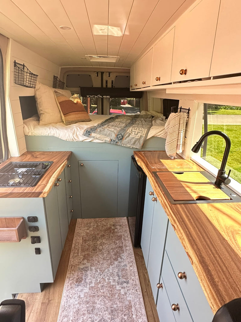 Cozy rv rental interior: light green cabinets, wood counters, compact kitchen with stove/sink, and a comfortable raised bed. — photo 2