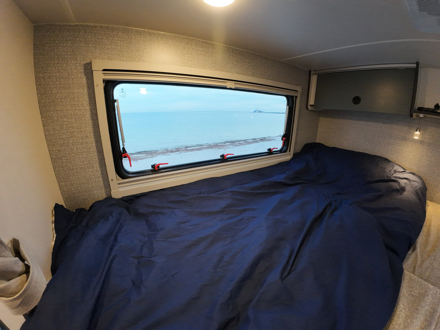 Experience comfort in this RV rental's bedroom, featuring a blue bed and a panoramic ocean view.