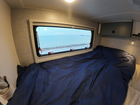 Experience comfort in this RV rental's bedroom, featuring a blue bed and a panoramic ocean view.