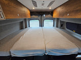 Experience comfort in this RV rental's cozy van interior. Features a plush bed, overhead storage, and rear windows.