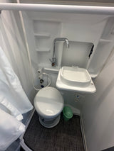 Compact RV rental bathroom featuring a toilet, small sink, and shower area with a curtain, maximizing space.
