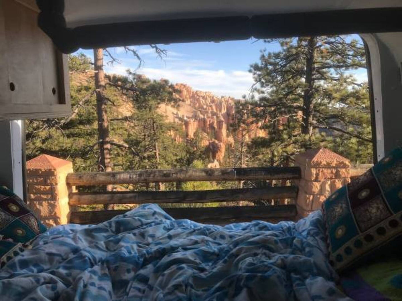 Enjoy a breathtaking Bryce Canyon view from a cozy RV rental bed, surrounded by majestic hoodoos and pine trees.