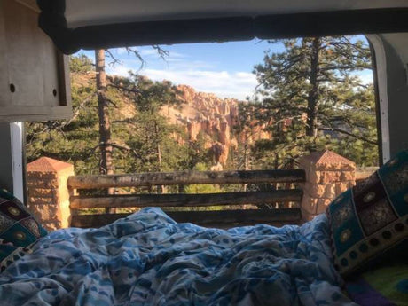 Enjoy a breathtaking Bryce Canyon view from a cozy RV rental bed, surrounded by majestic hoodoos and pine trees.
