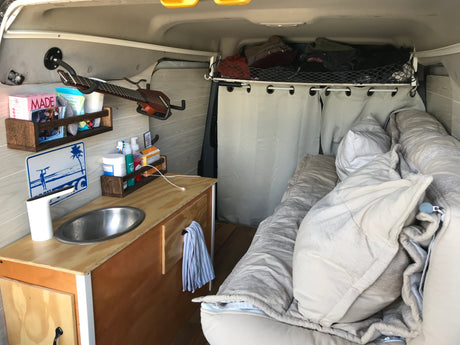 Inside an rv rental camper van: kitchenette with sink, cozy bed, shelves, guitar, & overhead storage for efficient living.