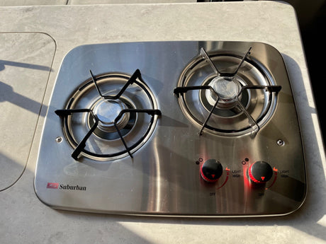 An integrated two-burner stainless steel stove by Suburban in an RV rental kitchenette, ready for cooking on the go.