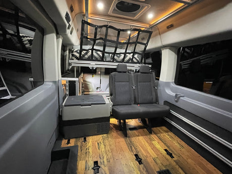 Spacious RV rental interior featuring comfortable seating, portable fridge, overhead bed, and attractive wood floor.