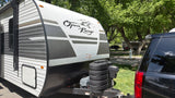 Front of an Open Range travel trailer, a great rv rental option, hitched to a black SUV in a sunny, green RV park.