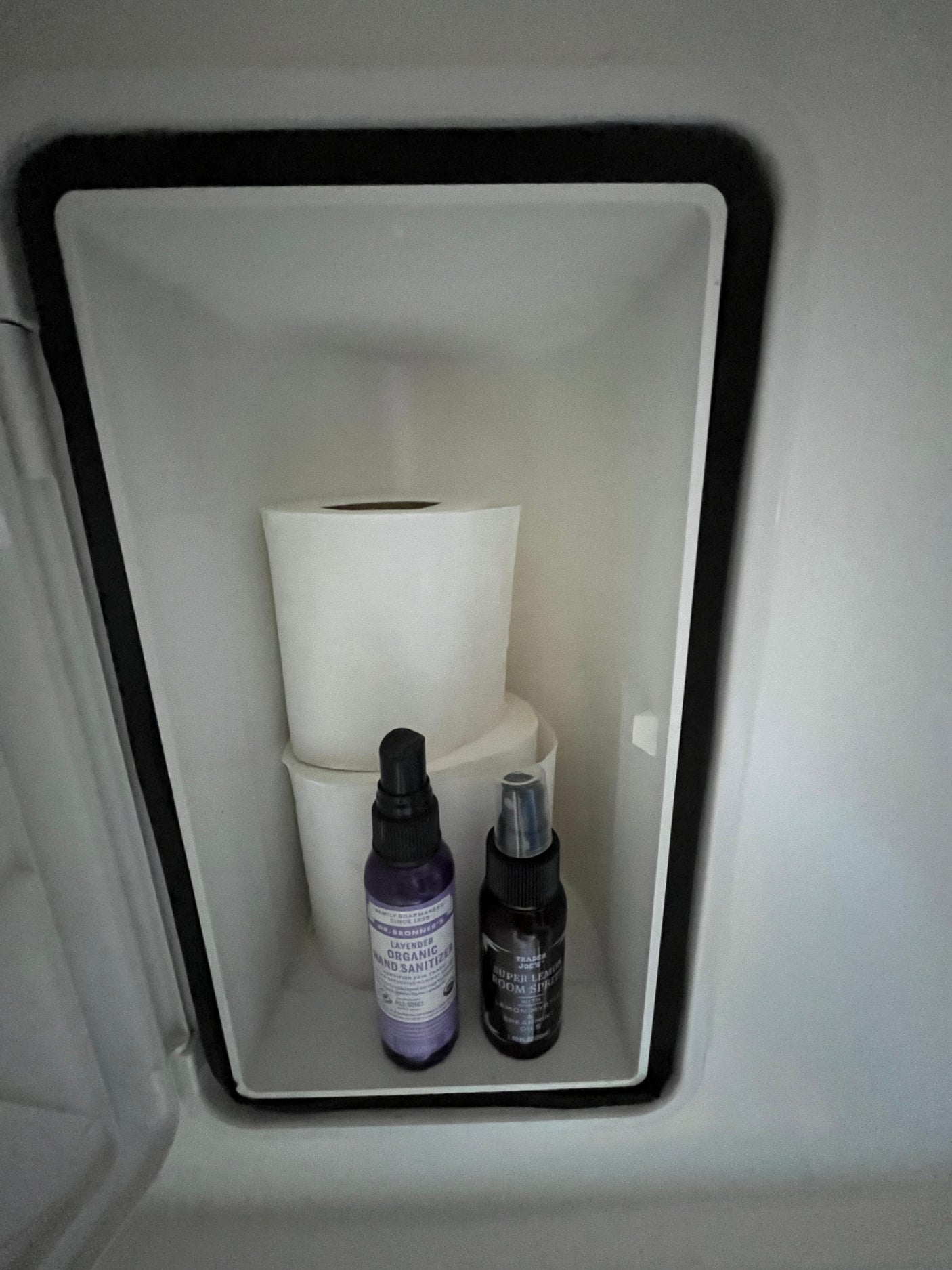 Compact RV rental storage holds essential hygiene items: toilet paper, hand sanitizer, and room spray.