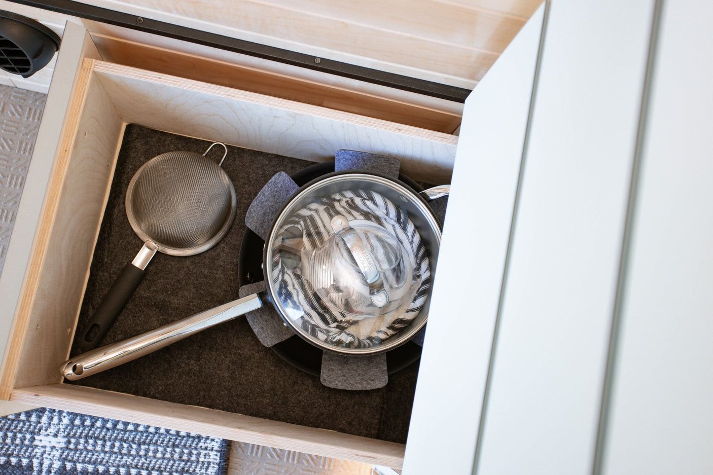 Open drawer in an RV rental, revealing neatly stored kitchenware: a lidded pot, strainer, and protective felt pads.