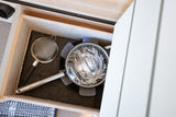 Open drawer in an RV rental, revealing neatly stored kitchenware: a lidded pot, strainer, and protective felt pads.