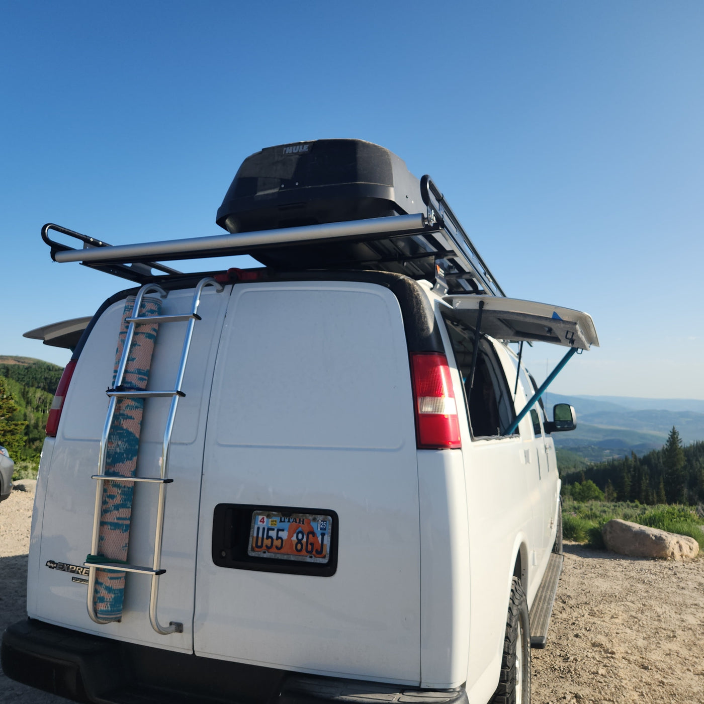 White van RV rental with roof box, ladder, and side awning, parked on a scenic overlook with mountains and blue sky. — photo 6