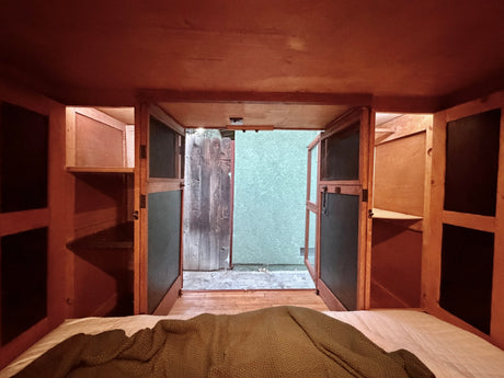 Cozy rv rental interior with a bed, wood accents, and an open door revealing an outdoor fence and green wall.