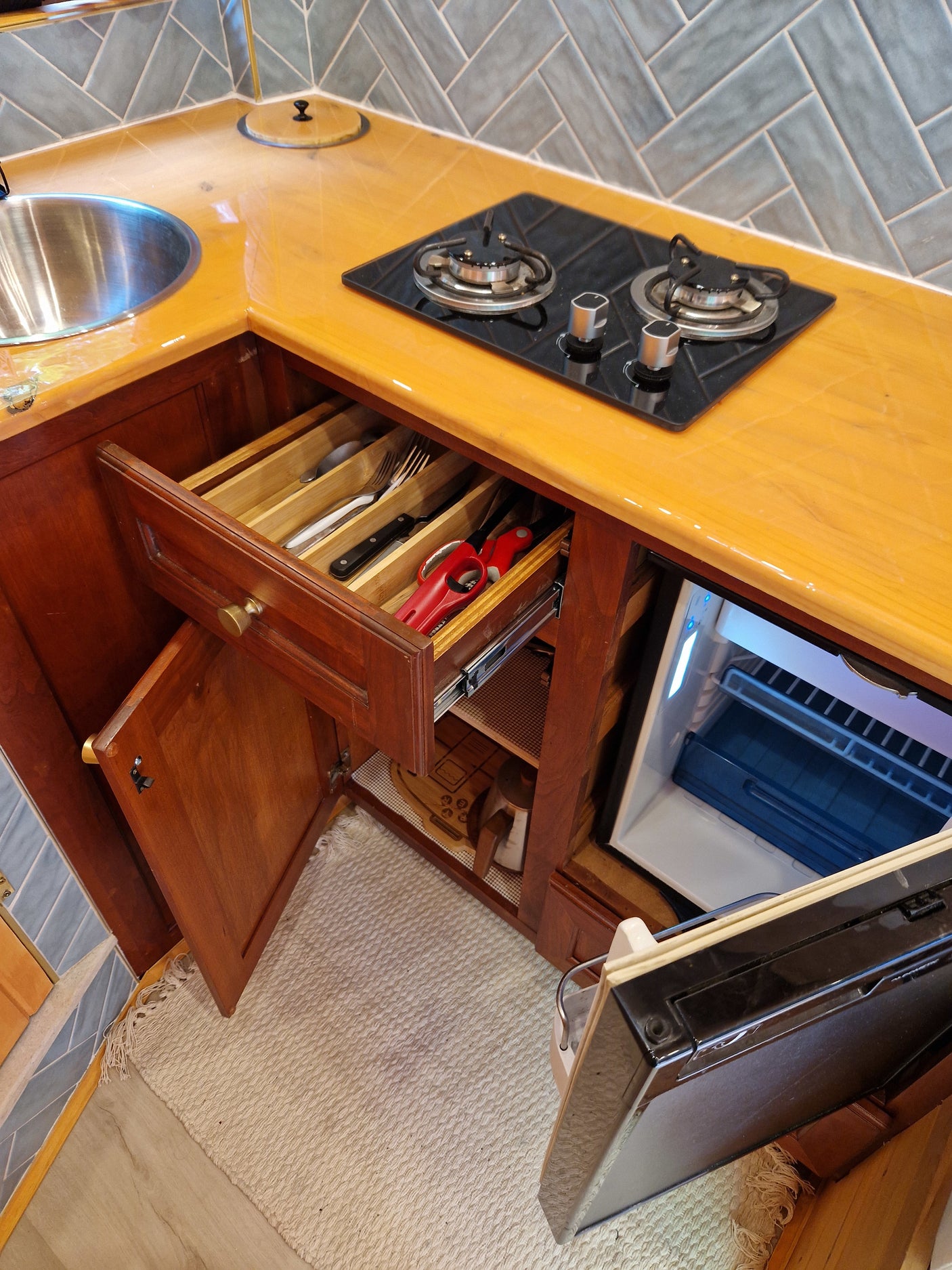 Organized compact kitchen in an RV rental, featuring a sink, 2-burner stove, utensil drawer, and mini-fridge.