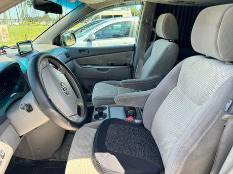 Inside an RV rental: light gray interior with dashboard, Toyota steering wheel, and patterned gray seats. Park view outside.