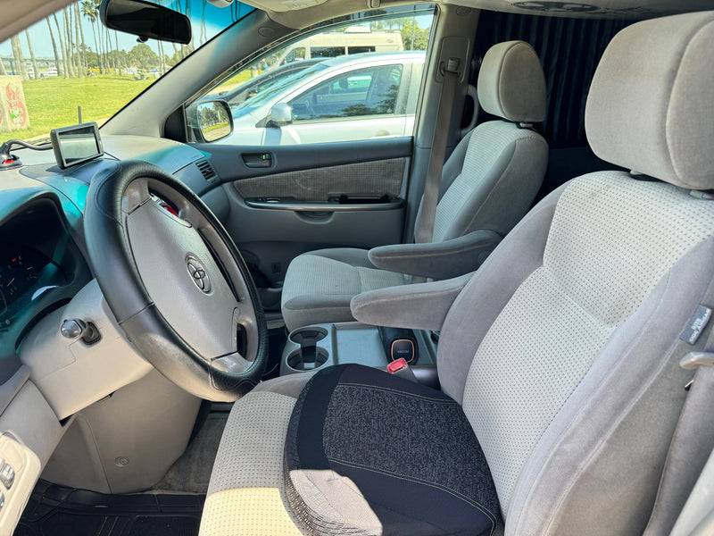 Inside an RV rental: light gray interior with dashboard, Toyota steering wheel, and patterned gray seats. Park view outside. — photo 5