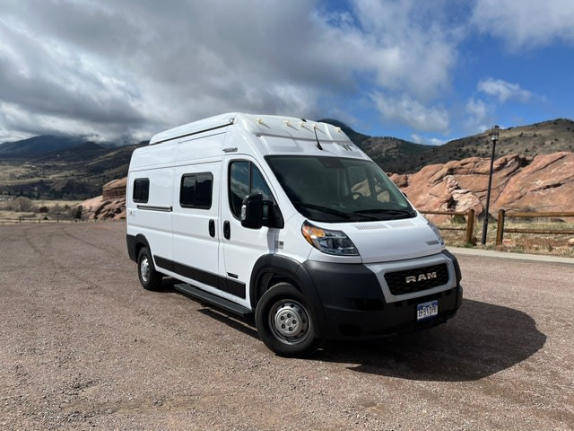 This white RV rental van is ready for outdoor travel, parked at a scenic red rock park with mountains in the background.