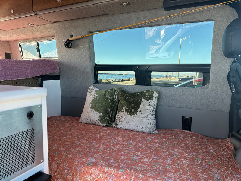 Cozy RV rental interior with a floral bed, textured pillows, and a fishing rod mounted above an ocean-view window. — photo 14
