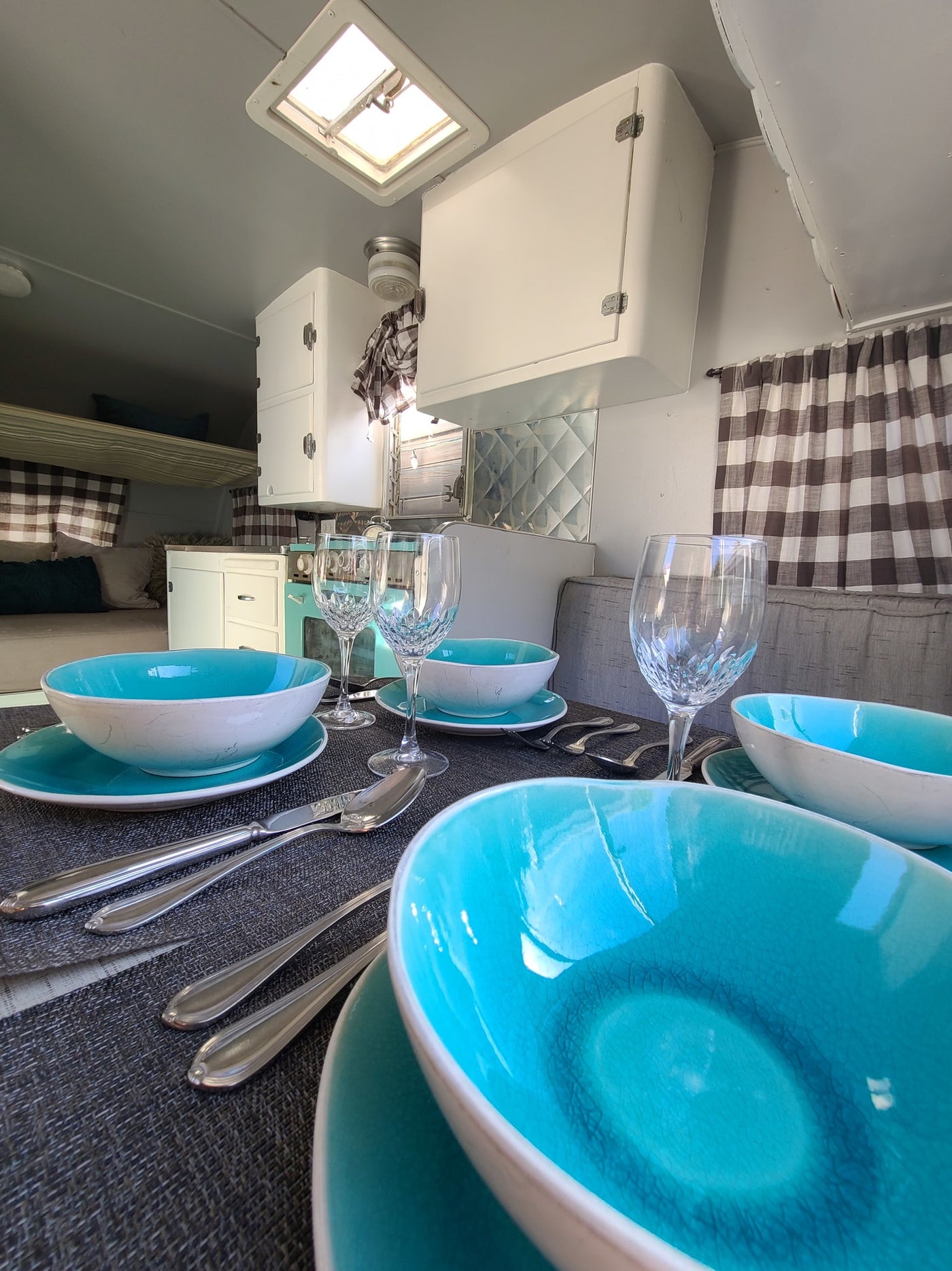 Charming RV rental interior: set dining table, kitchenette with aqua accents, and cozy bunk beds. Perfect for glamping! — photo 6
